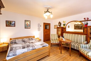 A cozy room with a wooden bed, a striped armchair, a small table with a bottle and glass, and a mirror above the sofa. - Pension Nostalgie - Minihotel (Cesky Krumlov)