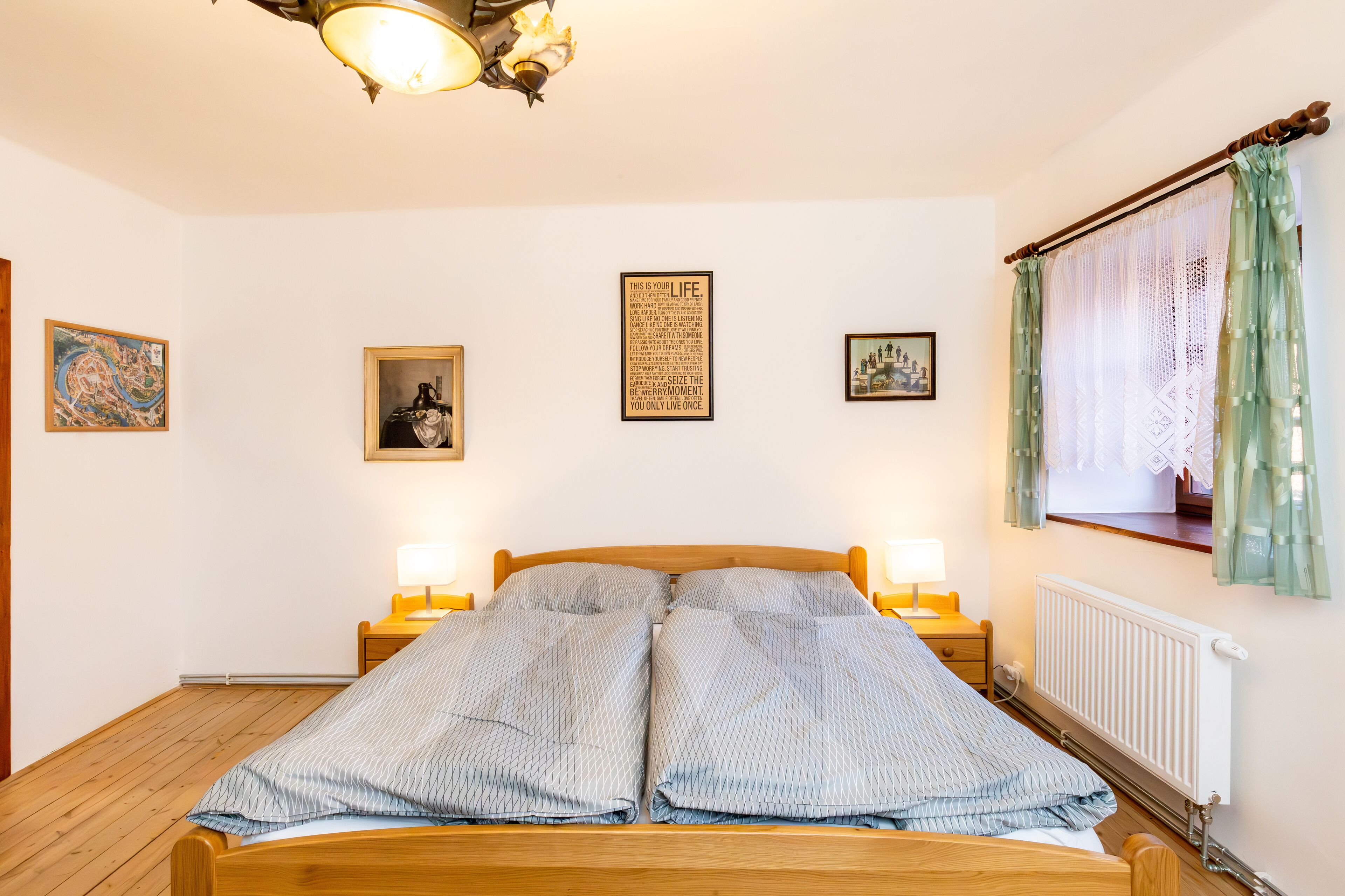 A neatly made bed with a wooden headboard, two bedside lamps, and a radiator.