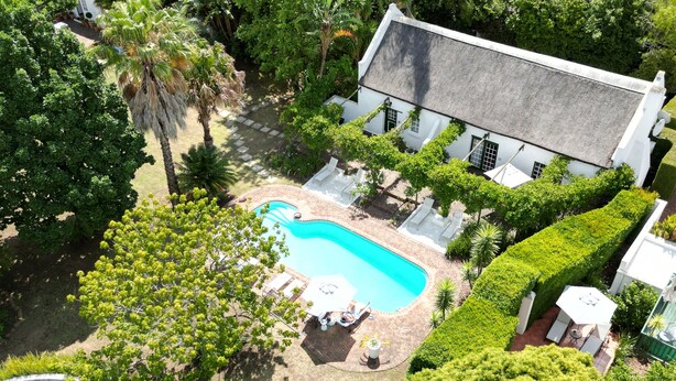 A swimming pool surrounded by white lounge chairs and a white building with a grey roof. - Rothman Manor Guest House (Swellendam)