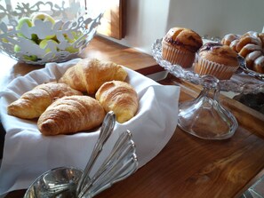 A wooden table with a white cloth, a glass bowl with green apples, and a glass stand with pastries.
