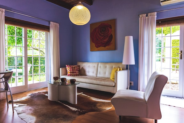A living room with a sofa, a coffee table, a chair, a lamp, and a painting of a rose on the wall.