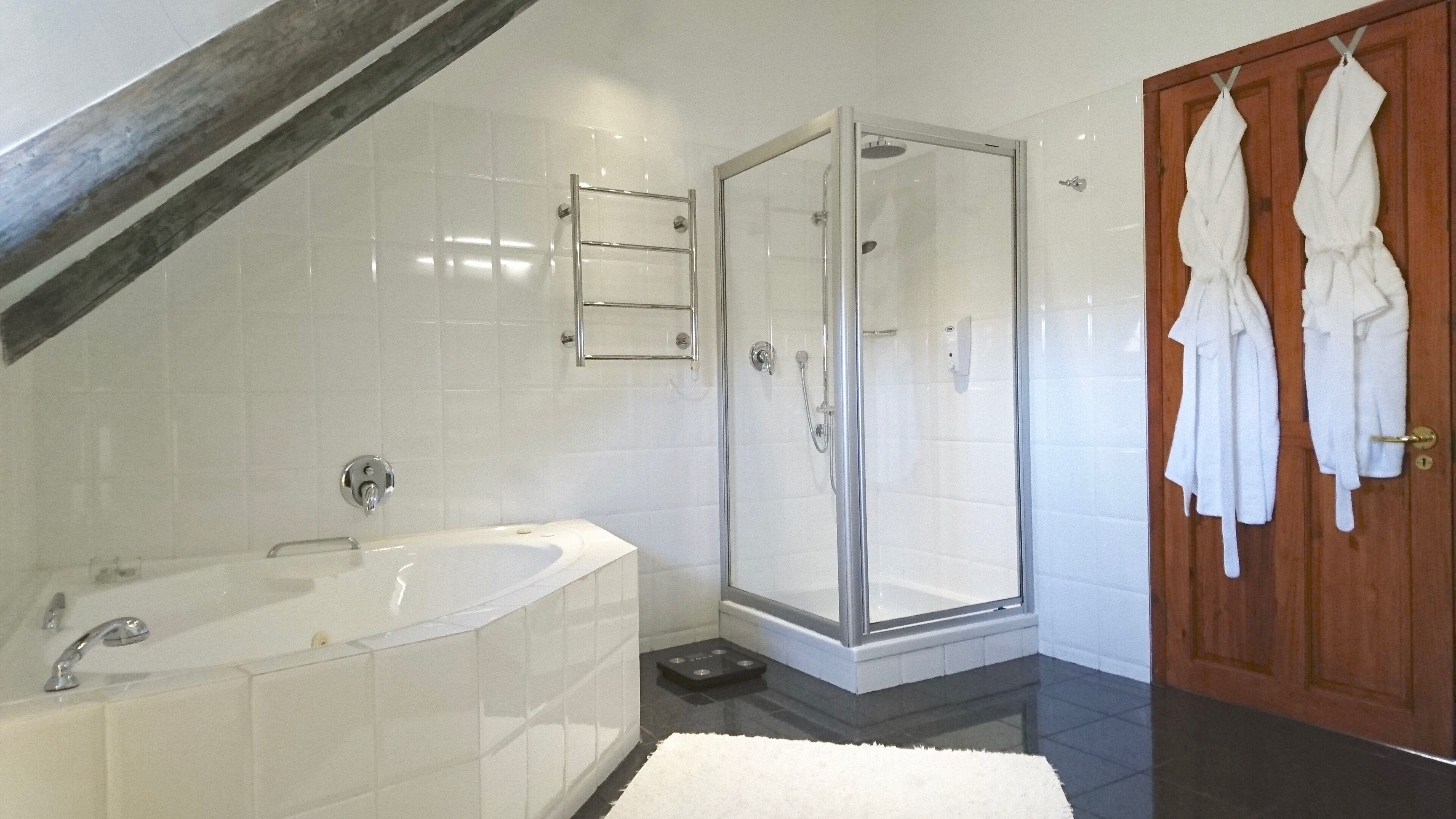 A modern bathroom with a freestanding bathtub, a glass-enclosed shower, and a wooden door.