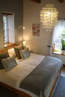 Quarto com cama grande, lustre, janela com cortinas e um vaso de planta.