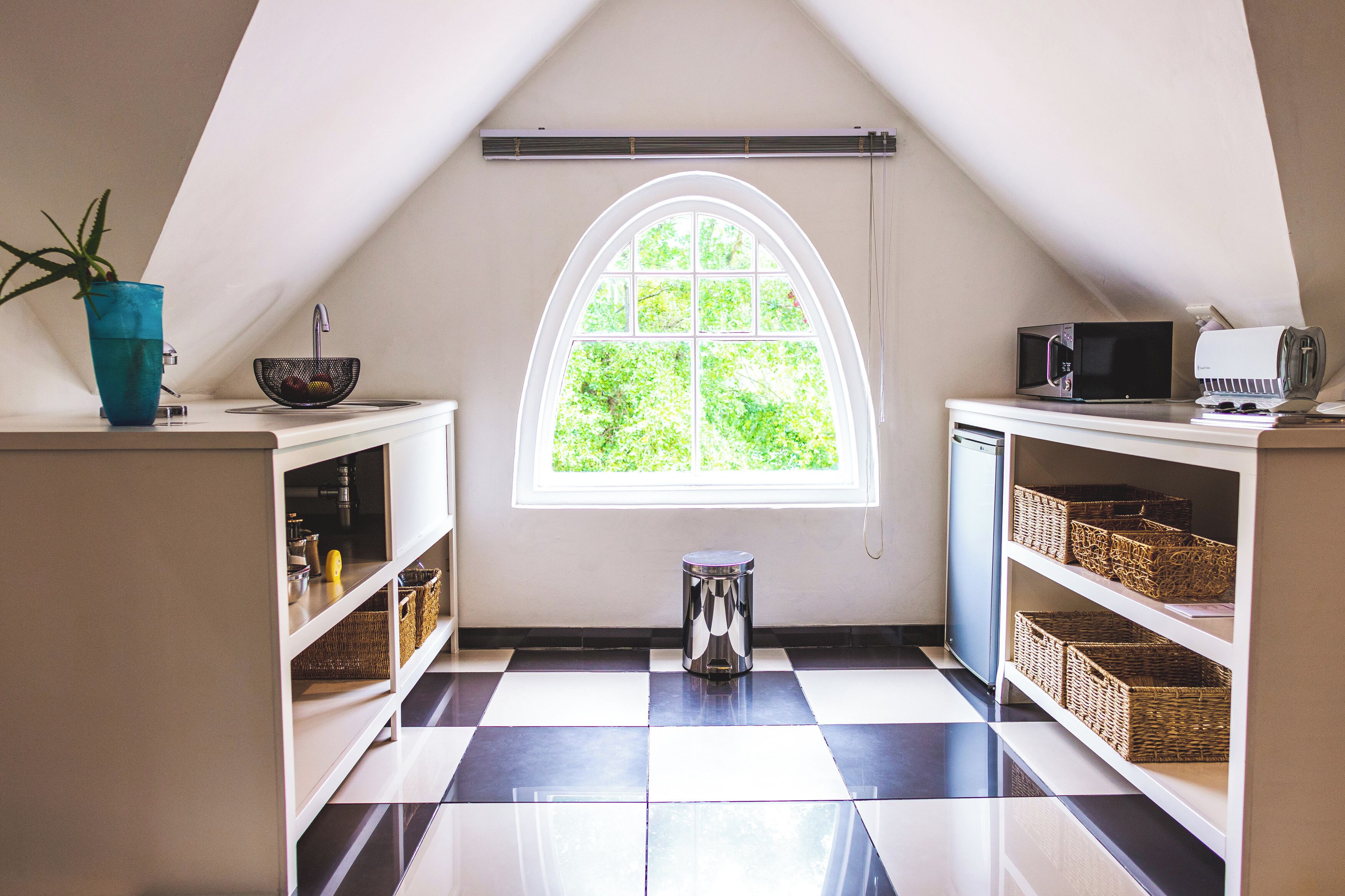 A kitchen with a checkered floor, a window with a view of greenery, and shelves with baskets.