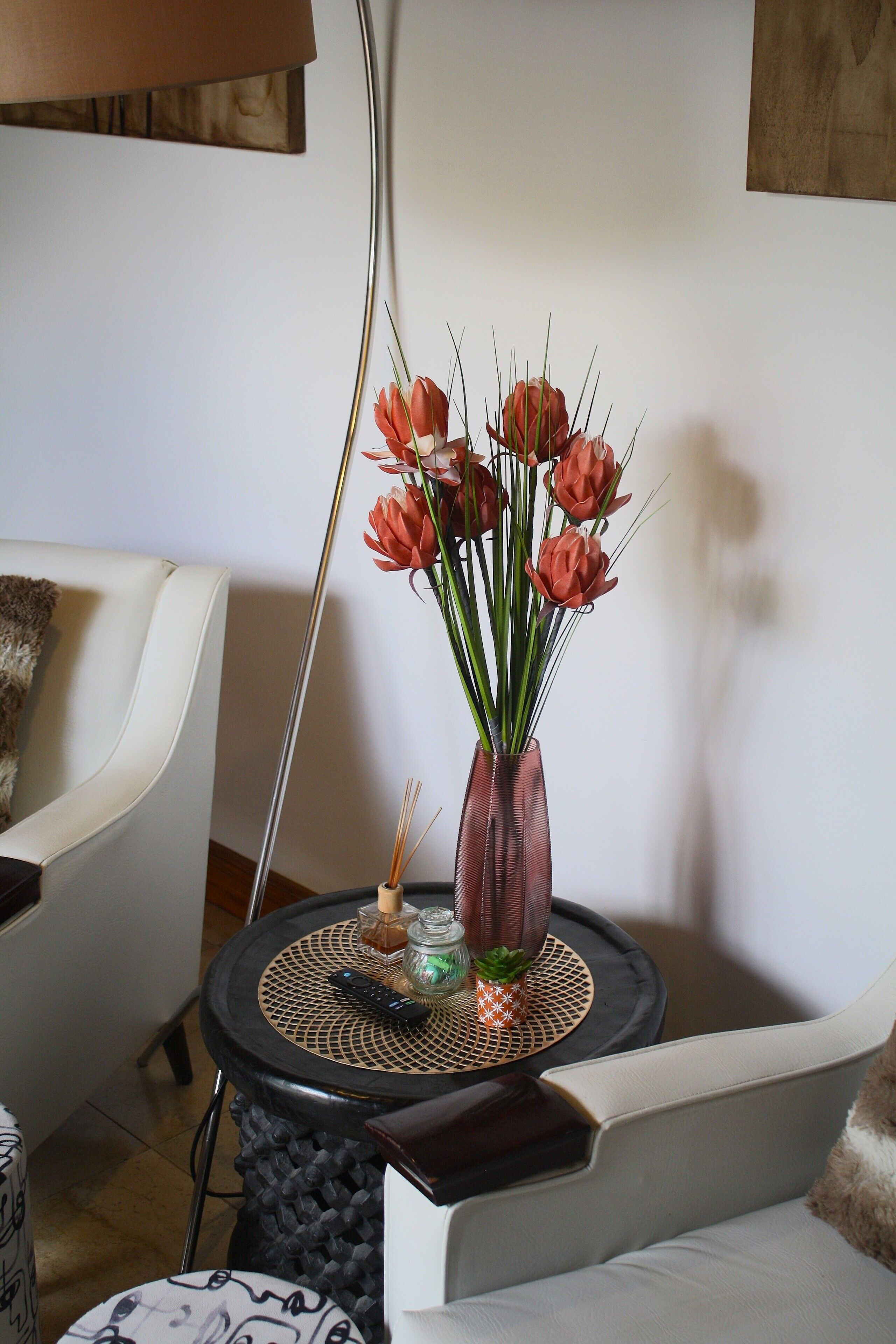 Ett modernt vardagsrum med en vit soffa, ett runt soffbord med en vas med röda blommor och en lampa.