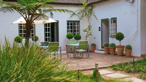 A courtyard with a table and chairs, surrounded by potted plants and a palm tree. - Rothman Manor Guest House (Swellendam)
