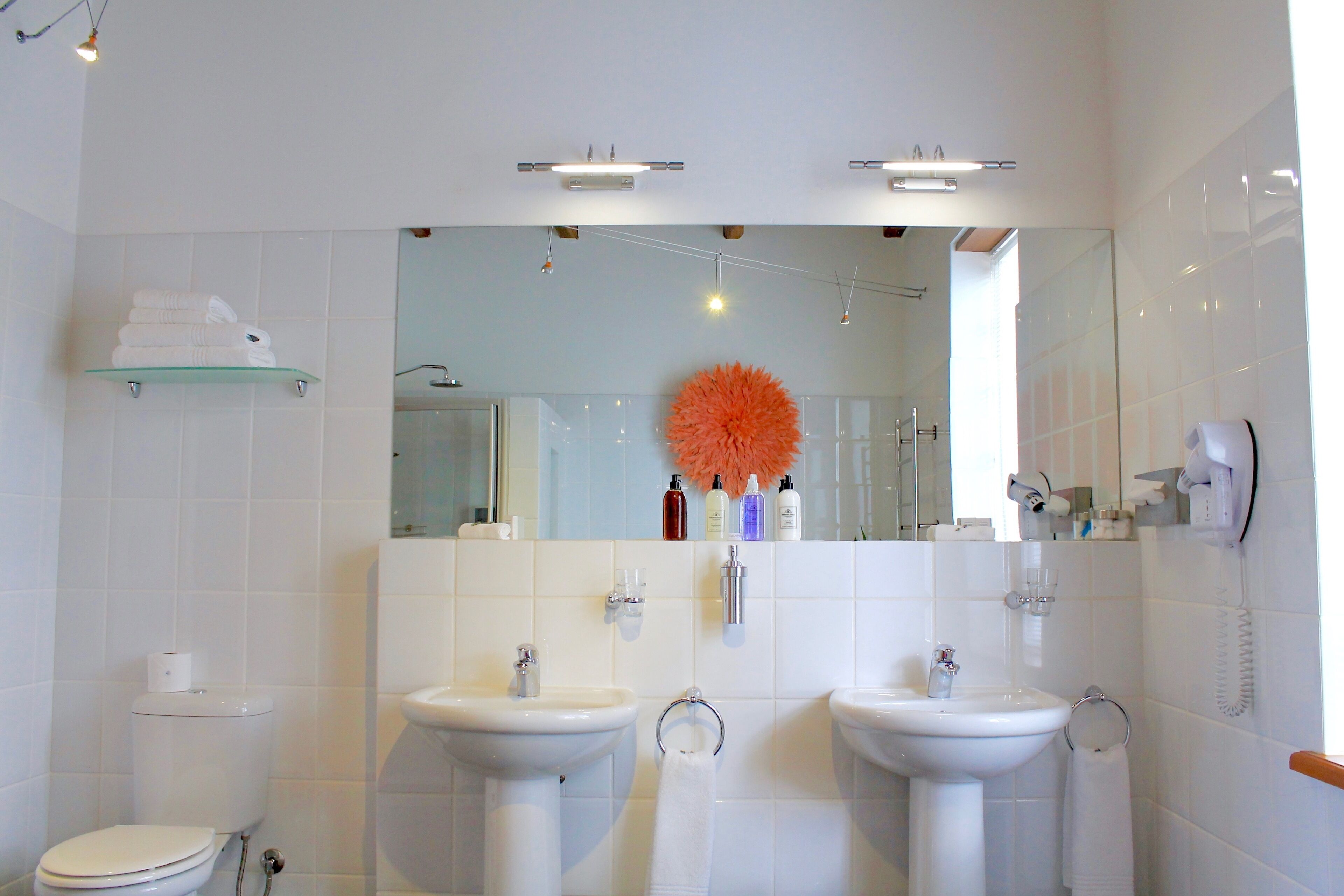 Un baño moderno con dos lavamanos, un inodoro y un estante de vidrio con toallas.