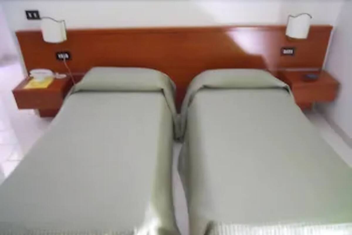 A hotel room with two single beds, a wooden headboard, bedside tables with lamps, and a small nightstand with a phone.