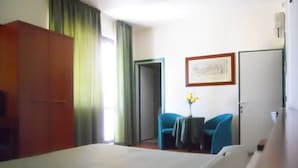 A hotel room with a bed, a desk, two chairs, a small table with a vase, and a door. - Hotel Traghetto (Civitavecchia)