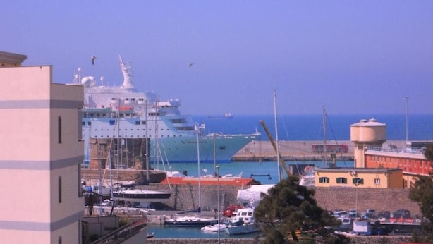 A marina with boats, a large cruise ship, and buildings in the background. - Hotel Traghetto (Civitavecchia)