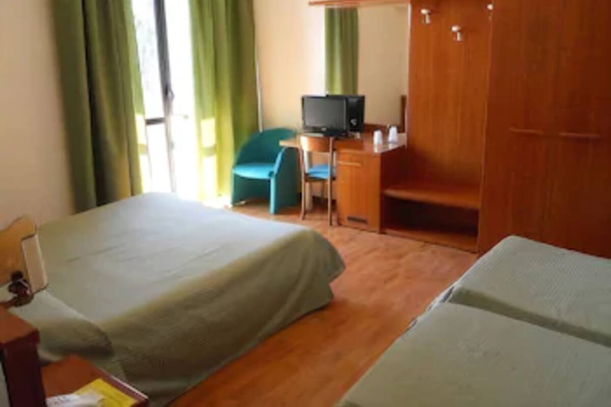A hotel room with two beds, a desk with a computer, a chair, and a wardrobe.