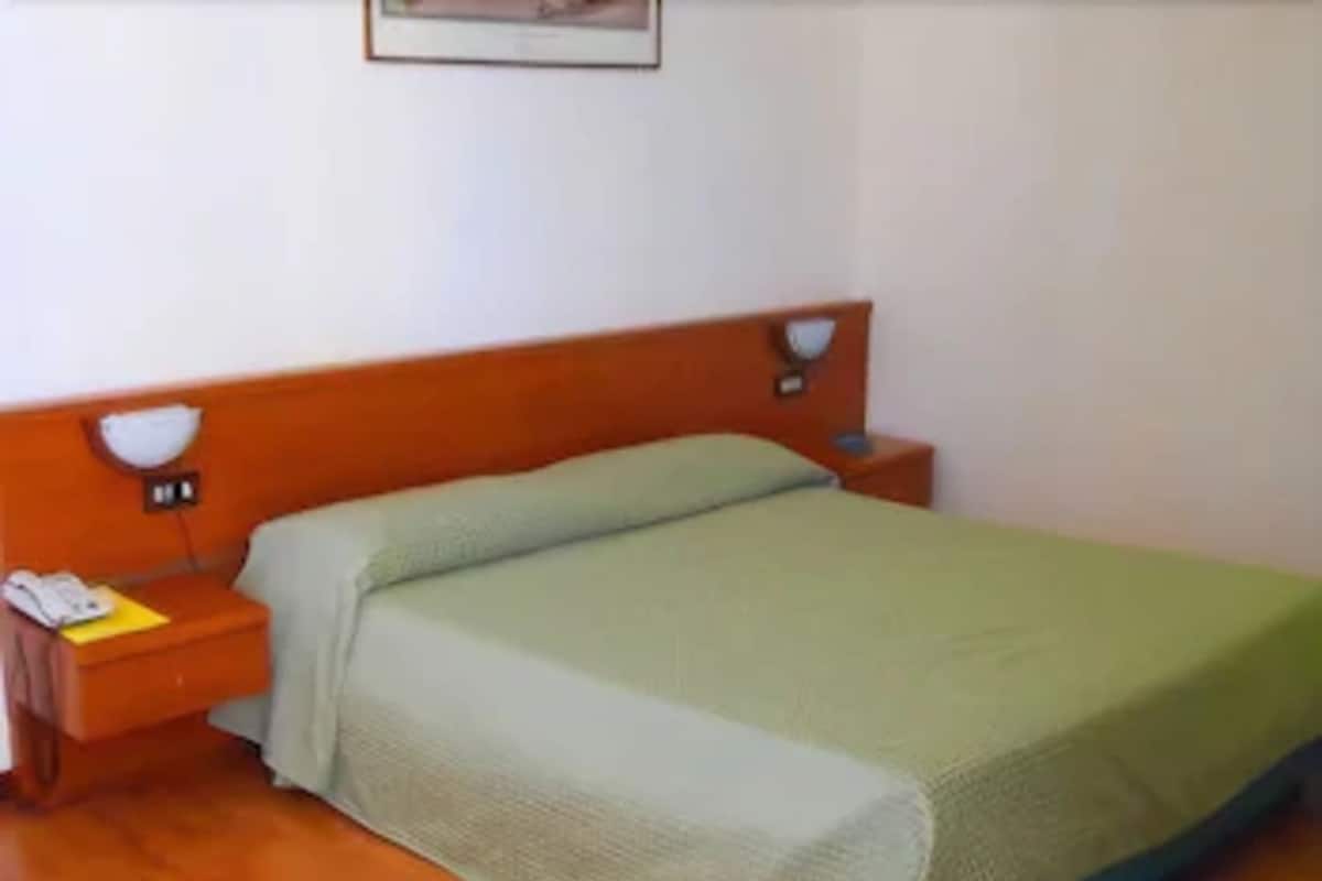 A single bed with a green bedspread in a room with wooden flooring and a white wall.