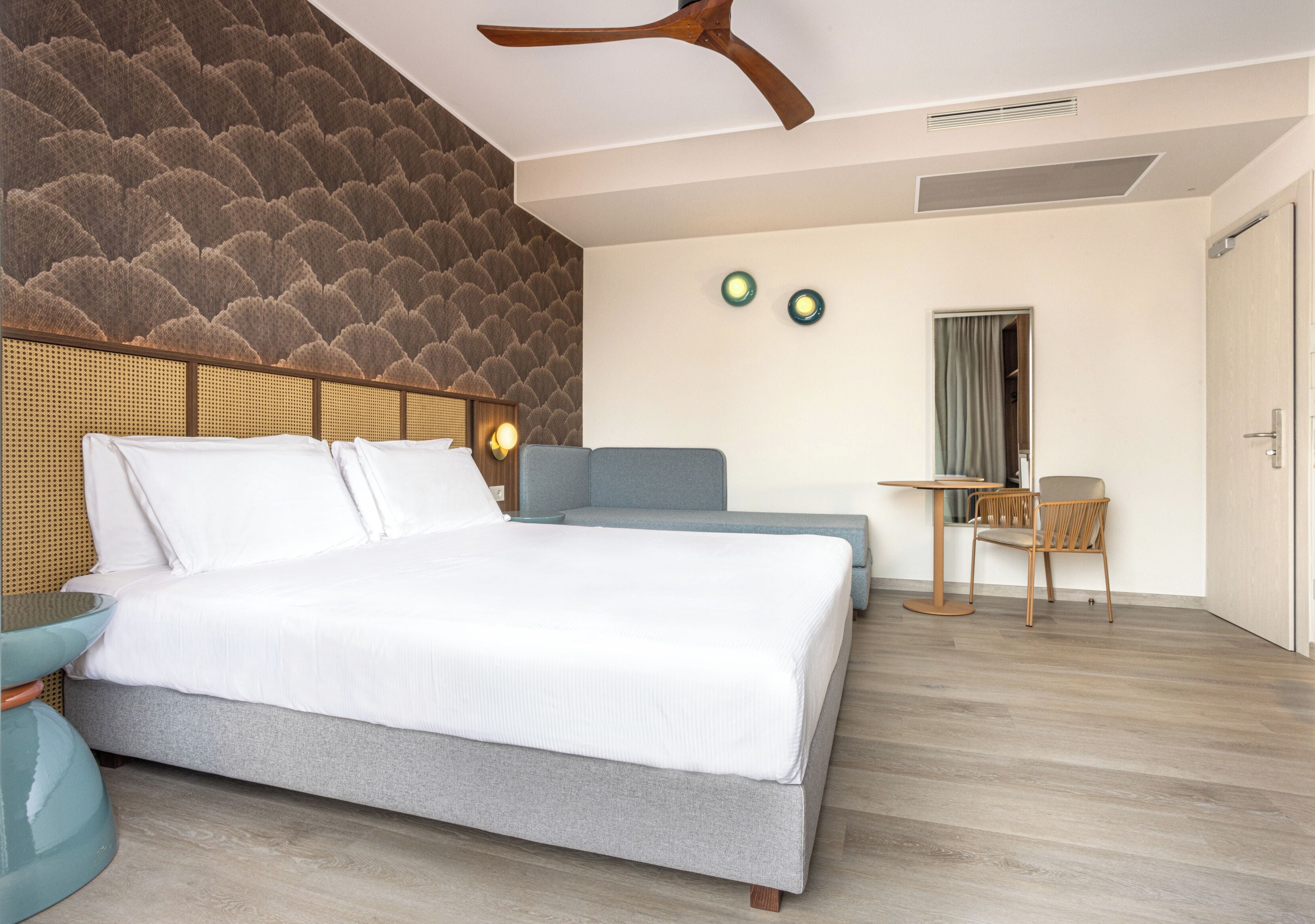 A modern hotel room with a large bed, a seating area with a table and chairs, and a ceiling fan.