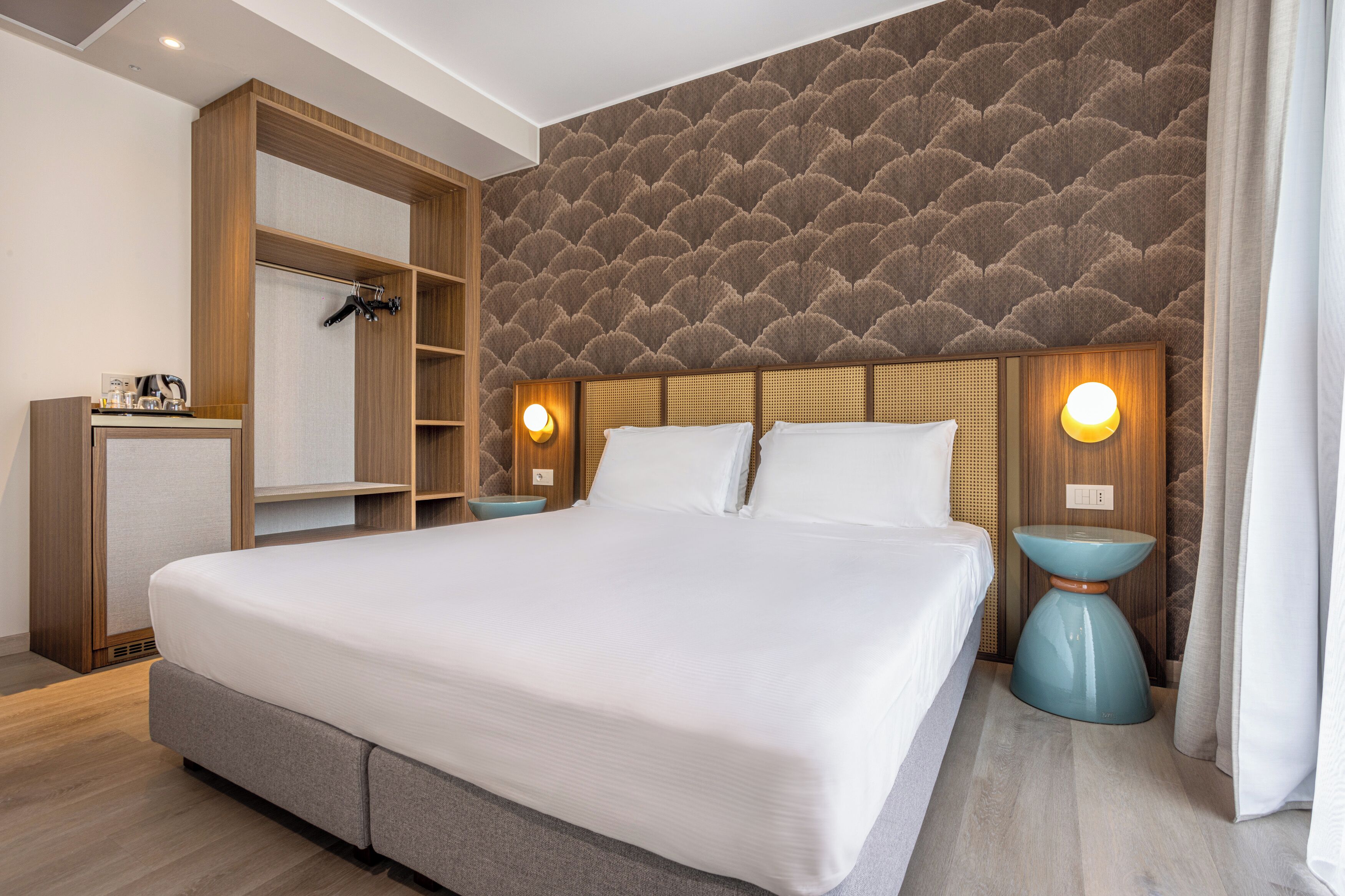 A modern hotel room with a large bed, wooden wardrobe, and a unique textured wall.