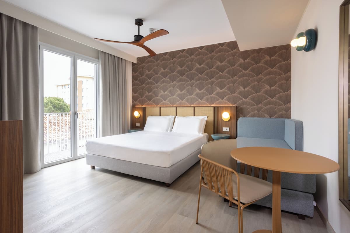 A modern hotel room with a large bed, a sofa, a small table, and a ceiling fan.
