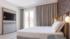 Habitación de hotel con cama, televisión, escritorio y vistas a edificios a través del ventanal.