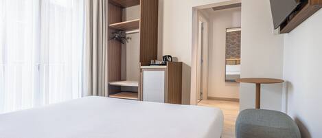 Habitación de hotel con una cama grande, un escritorio con una silla, un armario y un televisor instalado en la pared.