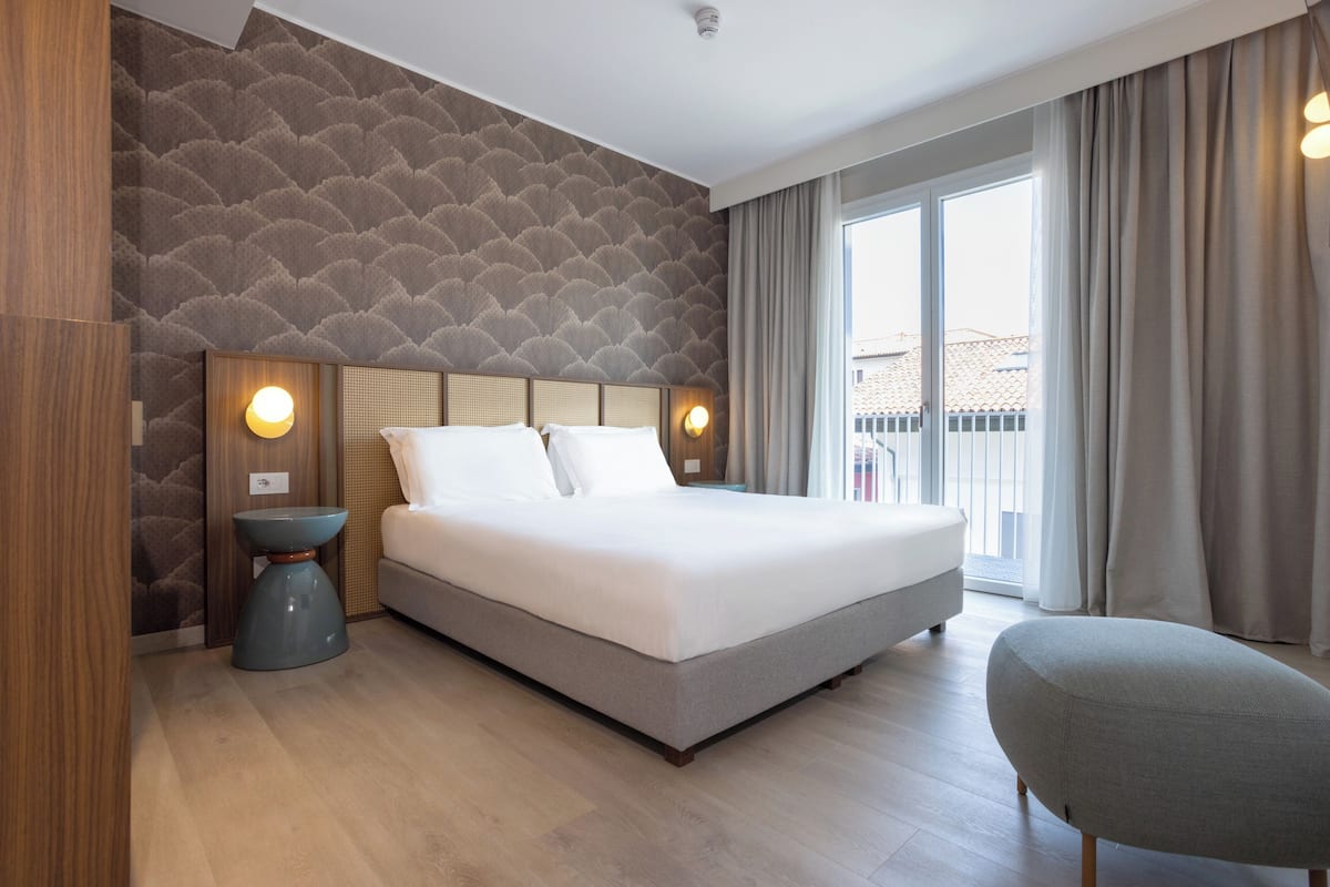 A modern hotel room with a large bed, a bedside table, and a chair.