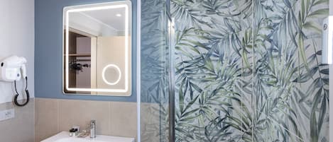 A bathroom with a white sink, a mirror with a light, and a shower with a tropical leaf wallpaper.
