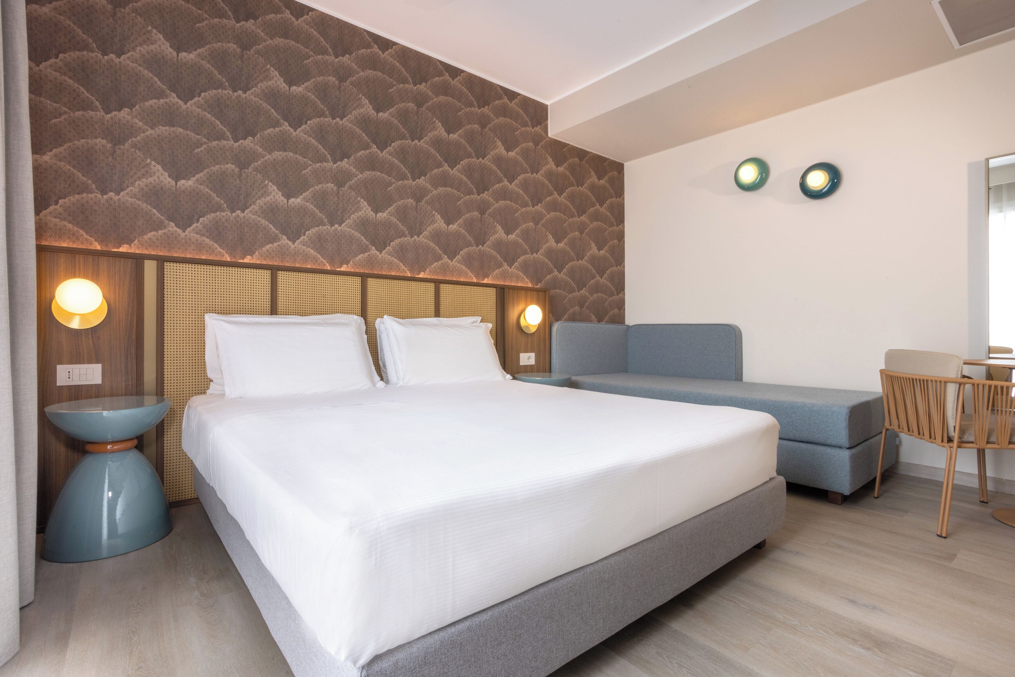 Una habitación de hotel moderna con una cama grande, un sofá, una mesita y dos lámparas de pared.