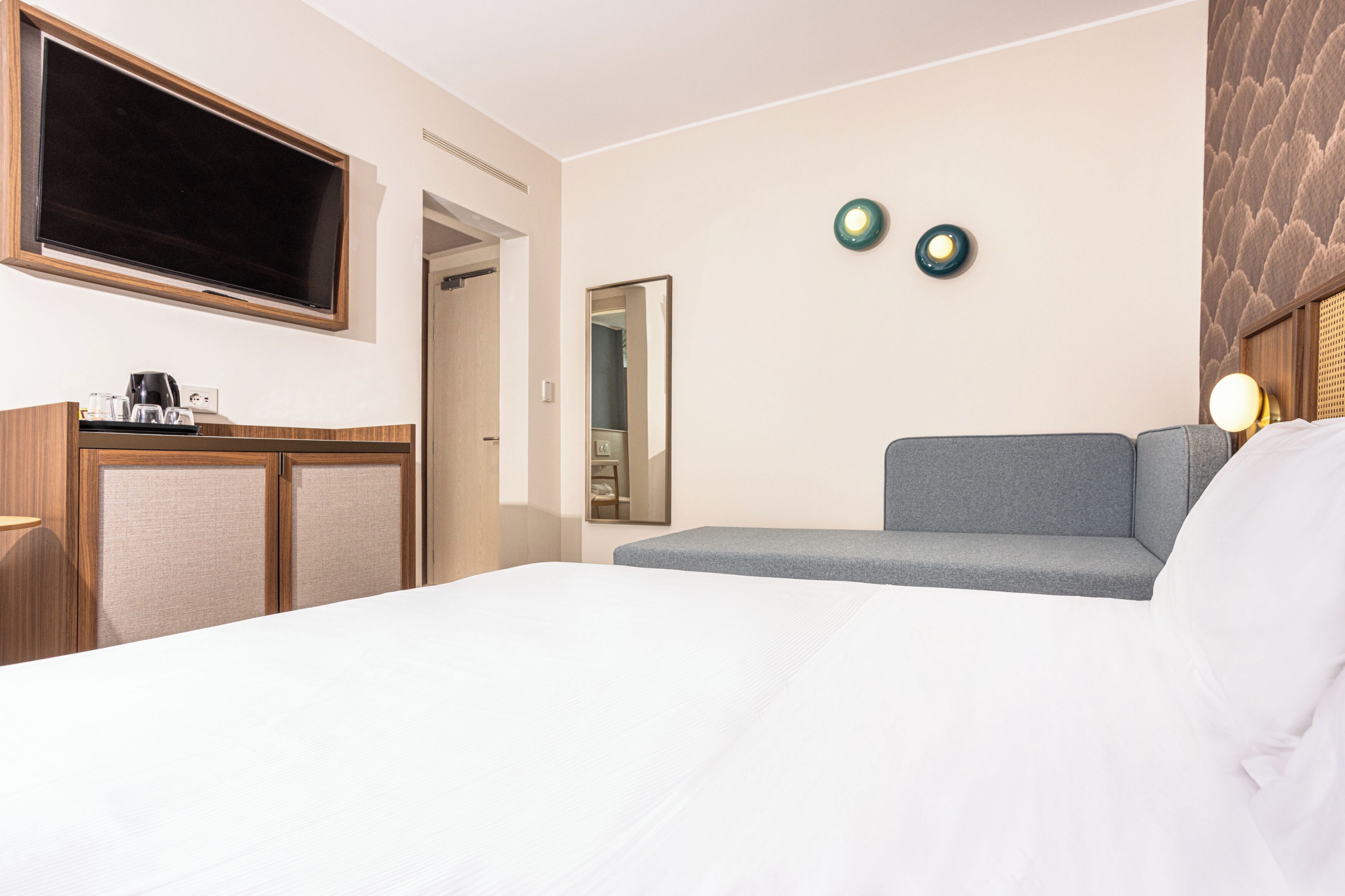 Una camera d'albergo con un letto, un divano, una TV, uno specchio e una macchina del caffè.