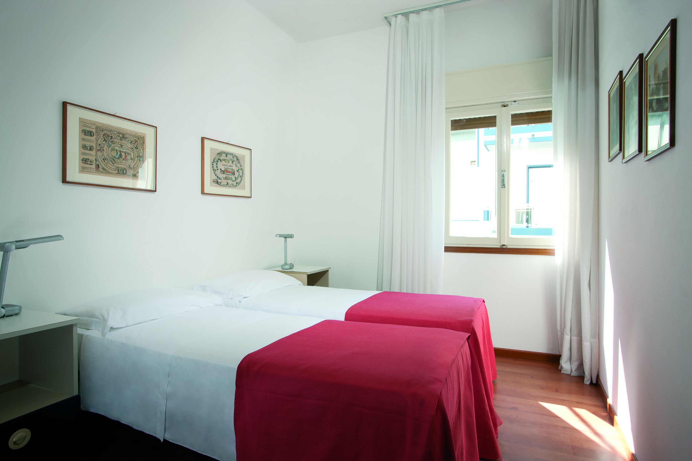 A hotel room with two beds, a nightstand, a lamp, and two framed pictures on the wall.
