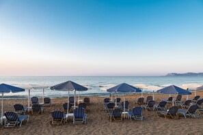 A beach with rows of sun loungers and striped umbrellas. - Lia Apartments (Chania)