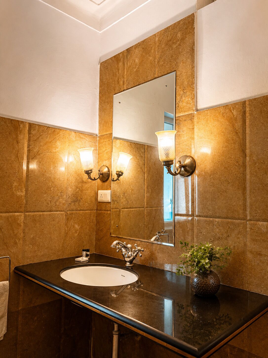 A bathroom with a marble wall, a sink with a single faucet, and two wall-mounted light fixtures.
