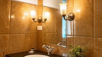 A bathroom with a marble wall, a sink with a single faucet, and two wall-mounted light fixtures.
