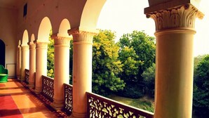 A covered corridor with white columns and arches, leading to a lush green garden.