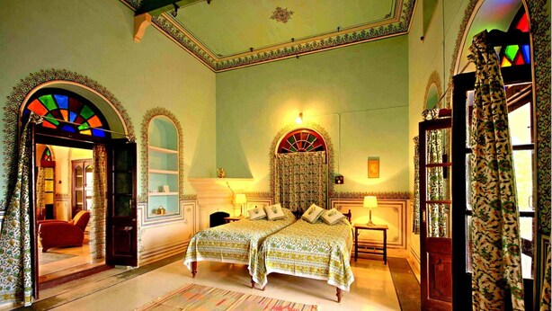 A traditional room with two beds, a large window with stained glass, and a patterned rug.