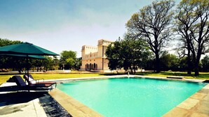 A swimming pool with lounge chairs and an umbrella, surrounded by a well-maintained lawn and a large tree.