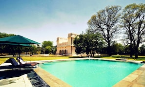 A swimming pool with lounge chairs and an umbrella, surrounded by a well-maintained lawn and a large tree.