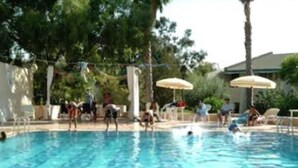Ein Schwimmbecken mit darin schwimmenden und spielenden Personen, umgeben von Bäumen und Sonnenschirmen.