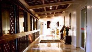 Ein Hotelkorridor mit einem gemusterten Teppich, einer dekorativen Decke und einem Empfangsbereich mit Theke und Stühlen.