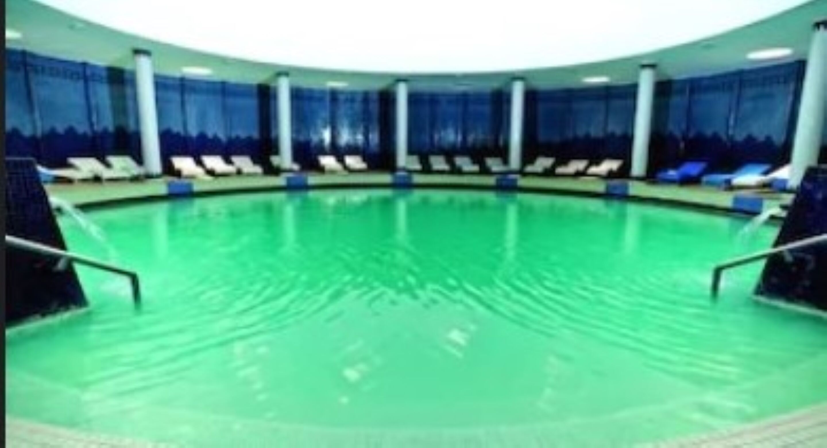 A large indoor swimming pool with multiple lanes, surrounded by lounge chairs and a covered seating area.