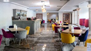 Um restaurante moderno com área de bar, cadeiras coloridas e piso de mármore.