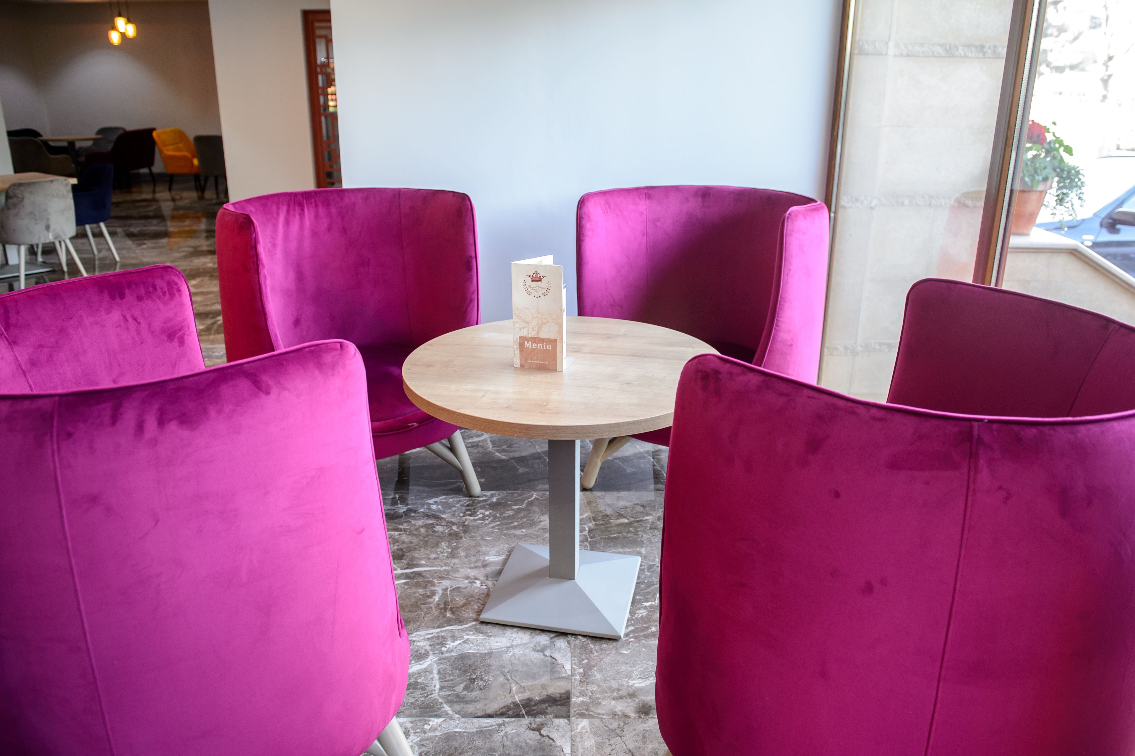 A seating area with four purple chairs around a small wooden table, a menu stand, and a stone floor.