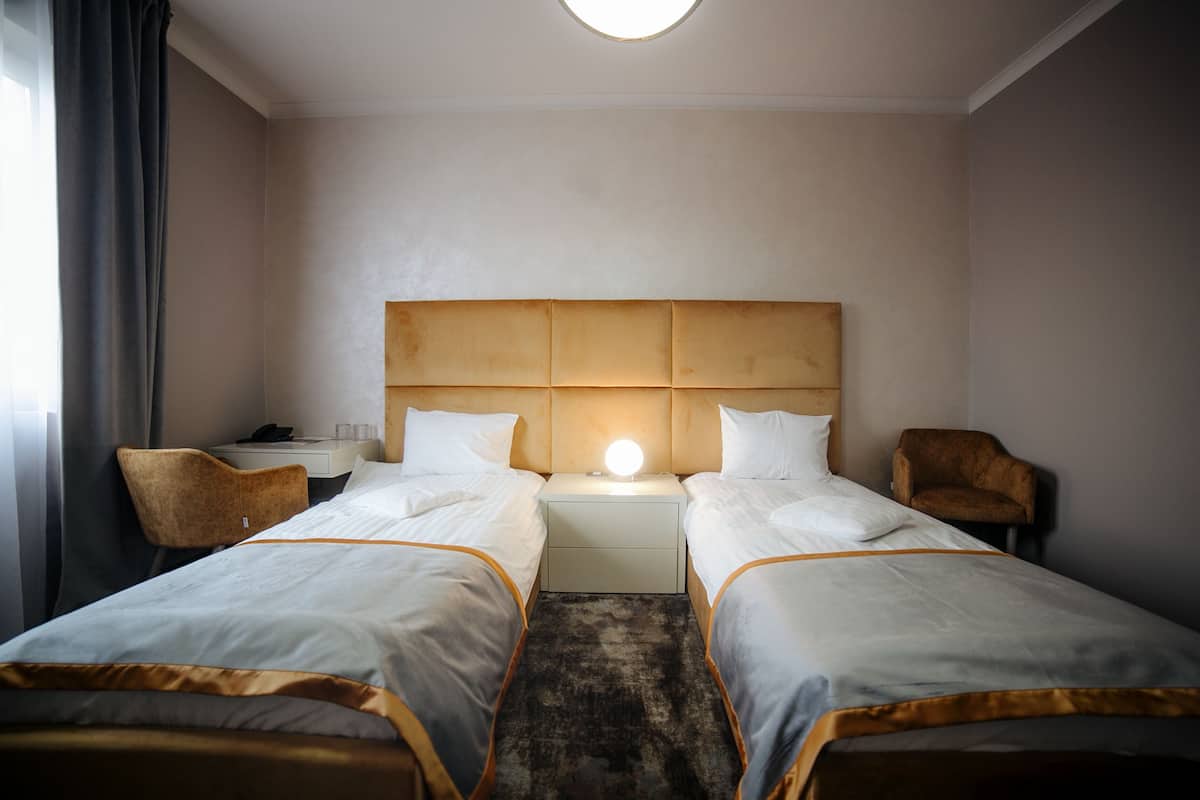 Une chambre d’hôtel avec deux lits simples, une table de chevet avec une lampe, une chaise et un bureau avec un téléphone et des lunettes.