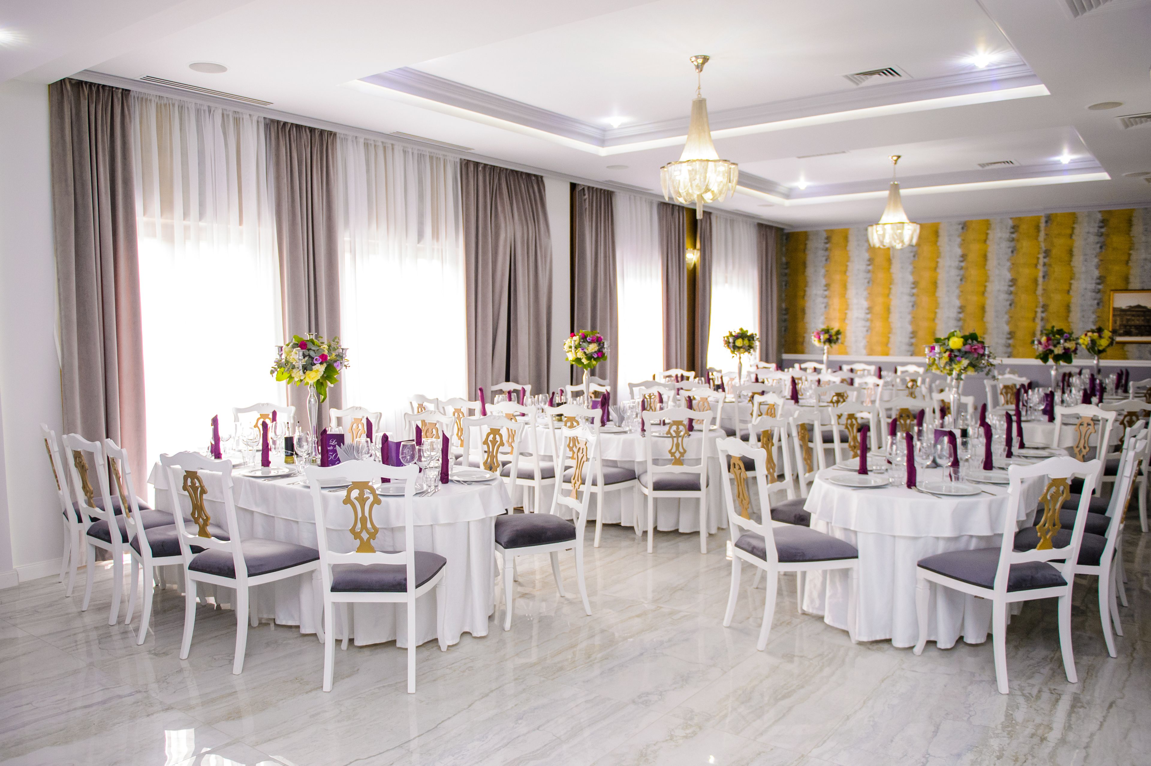 Une salle de banquet avec des tables rondes, des chaises blanches et des lustres.