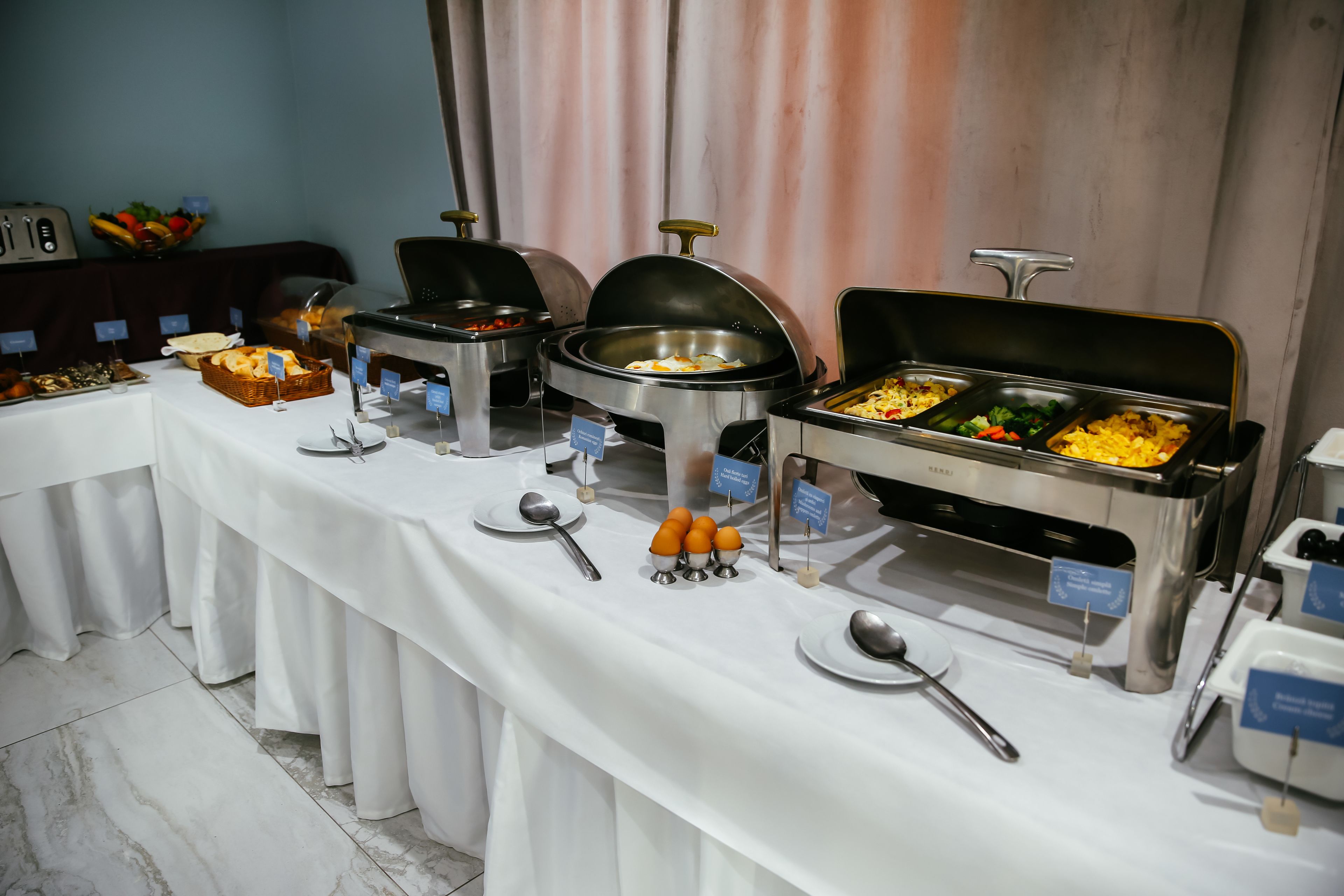 A buffet setup with various food stations, including a fruit bowl, a bread basket, and multiple serving containers.