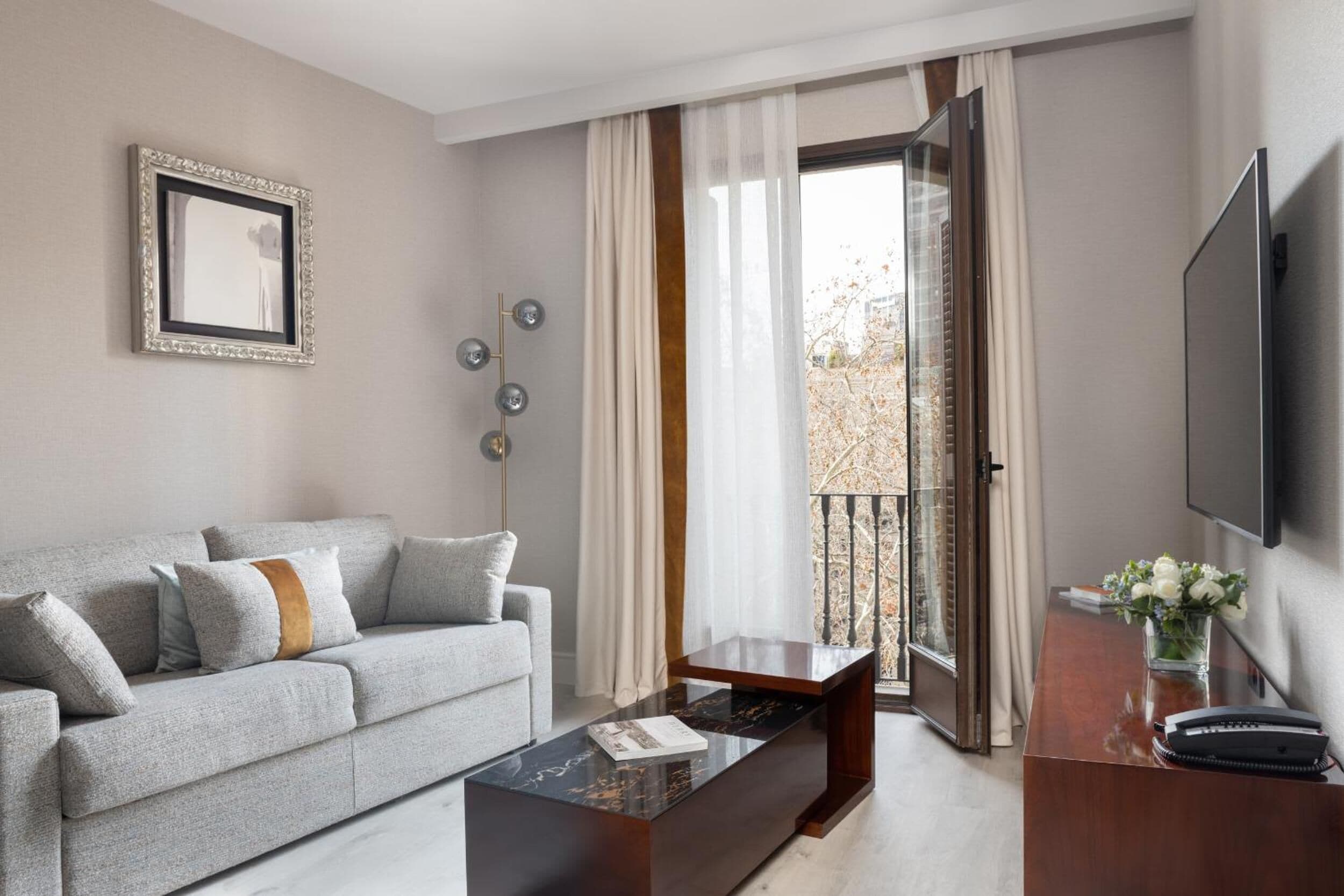 A modern living room with a grey sofa, a wooden coffee table, and a TV mounted on the wall.