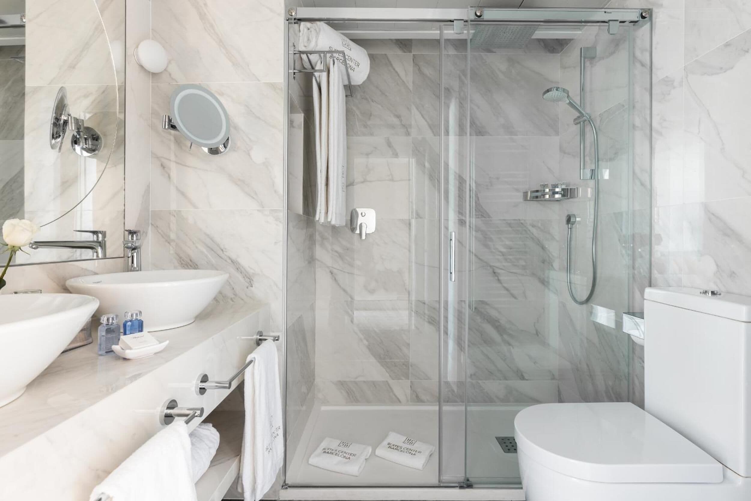A modern bathroom with a glass-enclosed shower, two sinks, and a toilet.