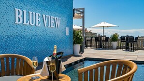 A poolside area with a blue mosaic wall labeled "BLUE VIEW," wooden chairs, a table with a bottle of champagne, and umbrellas. - Suites Center Barcelona (Barcelona)