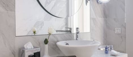 A modern bathroom with a large white sink, a glass vase with a white flower, and a tissue box on the counter.