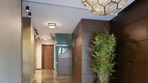 A modern hallway with a potted plant, recessed lighting, and a geometric ceiling light fixture. - Suites Center Barcelona (Barcelona)