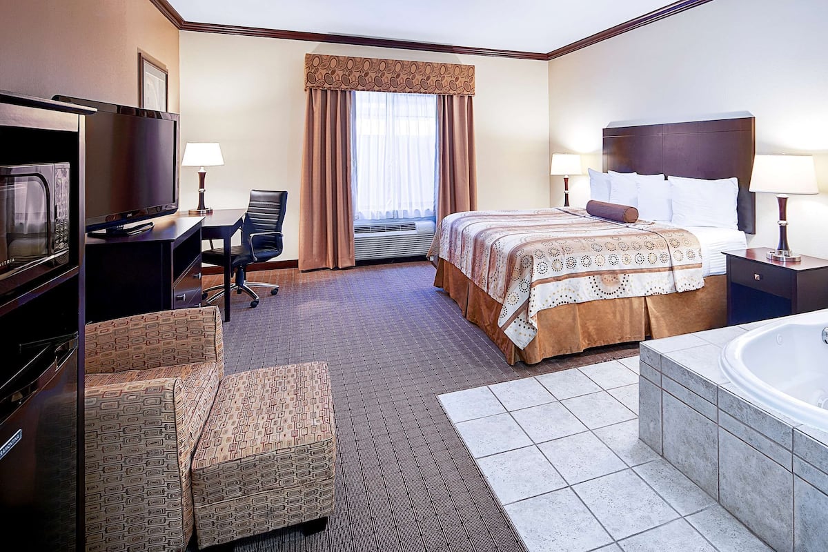 A hotel room with a bed, a desk, a chair, a TV, a bathroom with a bathtub, and a window with curtains.