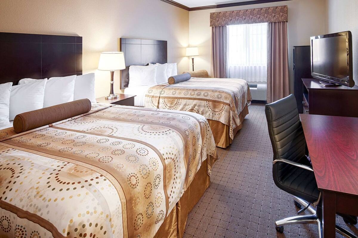 A hotel room with two beds, a desk, a chair, a television, and a window with curtains.
