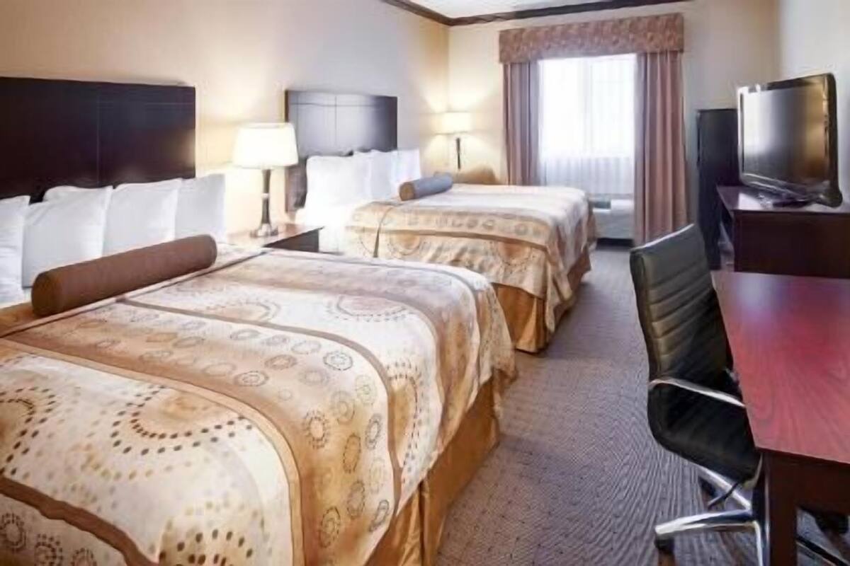A hotel room with two beds, a desk, a chair, a TV, and a window with curtains.