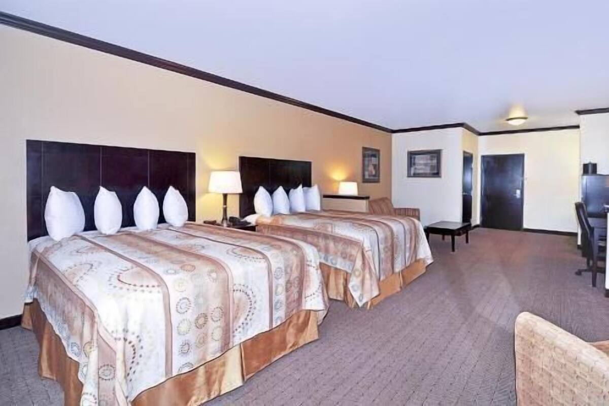 A hotel room with two beds, a desk, a chair, and a door.